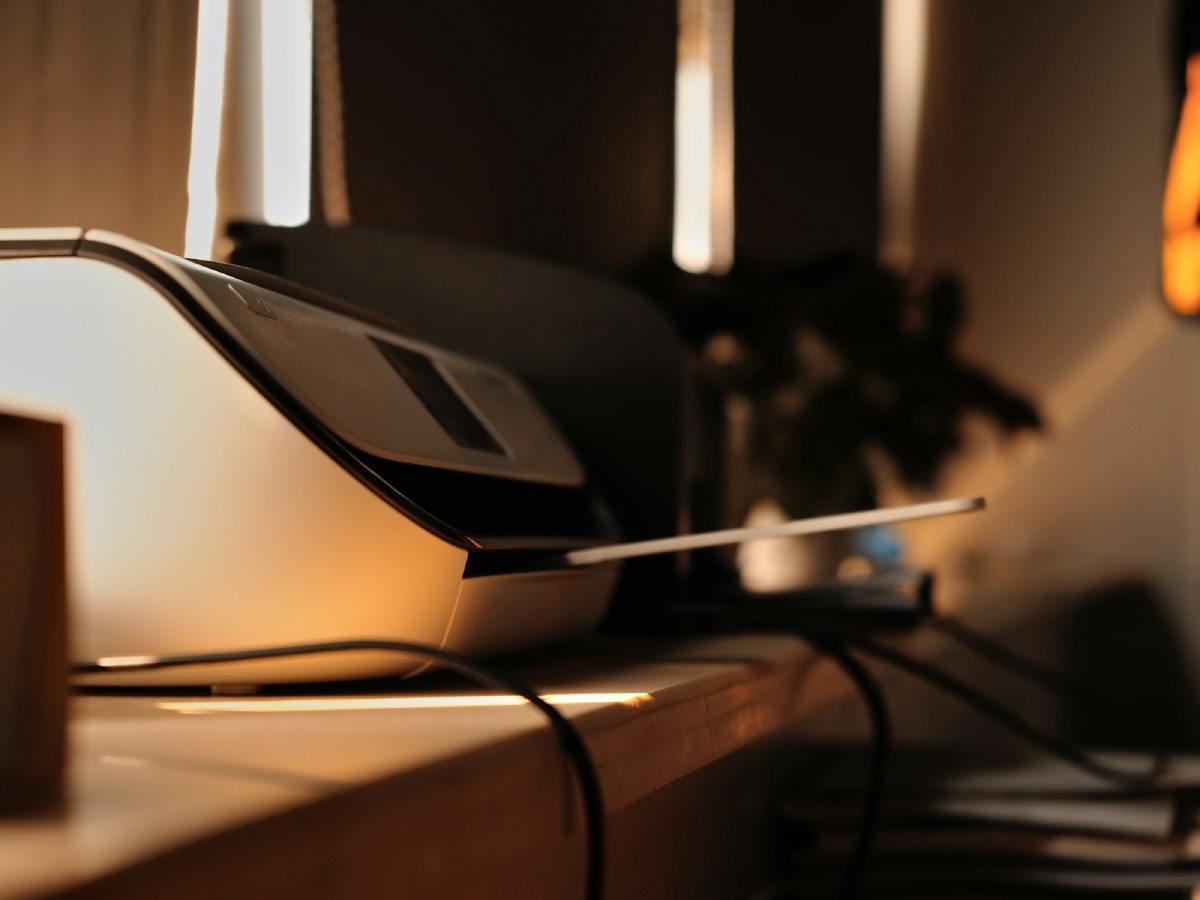 A multifunction office printer on a counter against a dark panelled wall